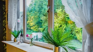 Una ventana con vistas a la vegetación, una mesa con un jarrón de flores y una botella de vino.