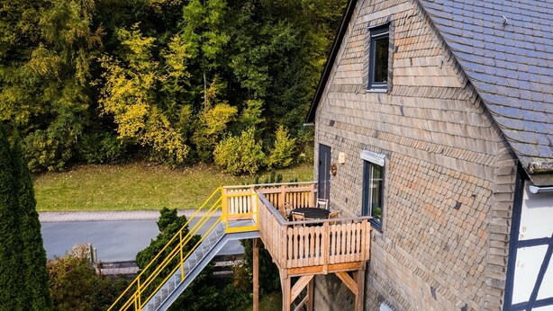 Una casa a due piani con un patio in legno e una scala che conduce a un balcone.
