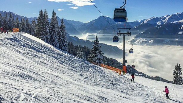 Un télésiège transportant des skieurs, une pente de montagne enneigée et un ciel dégagé.