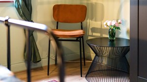 Een kamer met een stoel, een klein rond tafeltje en een vaas met bloemen.