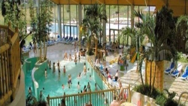 Una piscina interior con múltiples carriles, rodeada de áreas de descanso con sillas y mesas.
