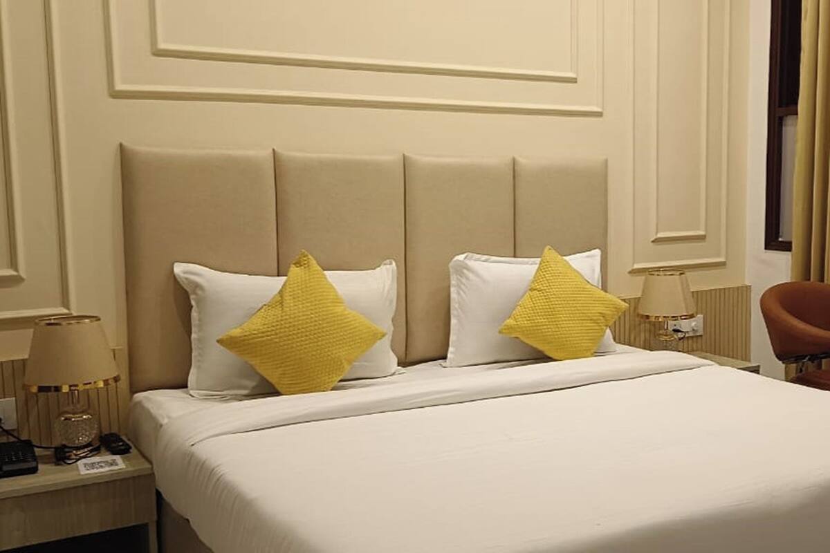 Een hotelkamer met een bed, twee kussens, een nachtkastje met een lamp en een stoel.