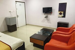 A hotel room with a bed, a glass-top coffee table, a red sofa, a TV, a mirror, and a small cabinet. - Hotel Diamond Park, Madhapur (Hyderabad)