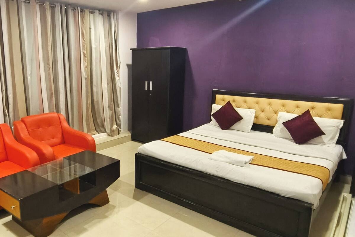 A hotel room with a bed, a red sofa, a black wardrobe, and a glass coffee table.
