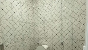 A bathroom with a toilet, a trash bin, and tiled walls. - Medina House Syariah Aceh (Banda Aceh)