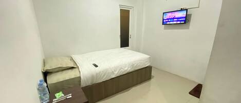 A small, clean room with a bed, a TV mounted on the wall, and an air conditioning unit.