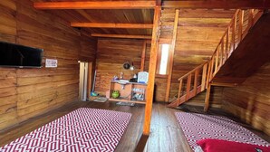 Interieur van een houten chalet met een houten trap, een flatscreen televisie aan de muur en een klein kitchenettegedeelte.
