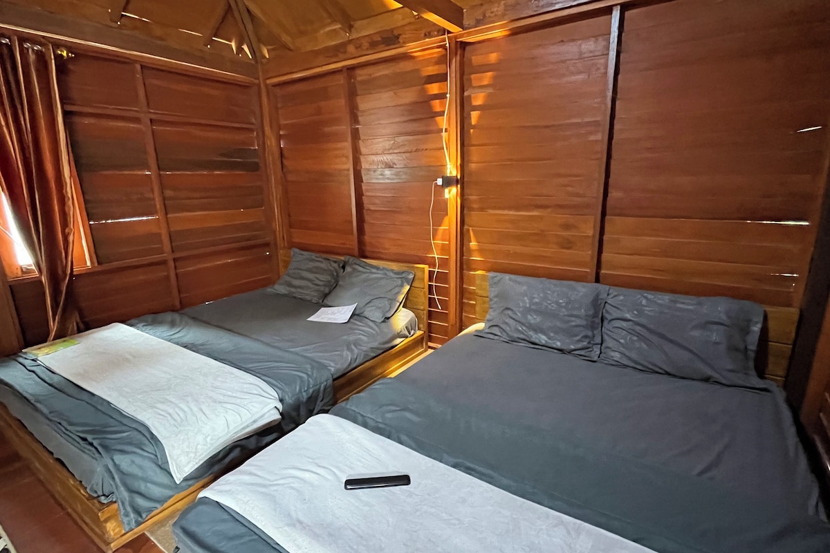 A wooden cabin room with two beds, each with grey bedding and a remote control on one bed.