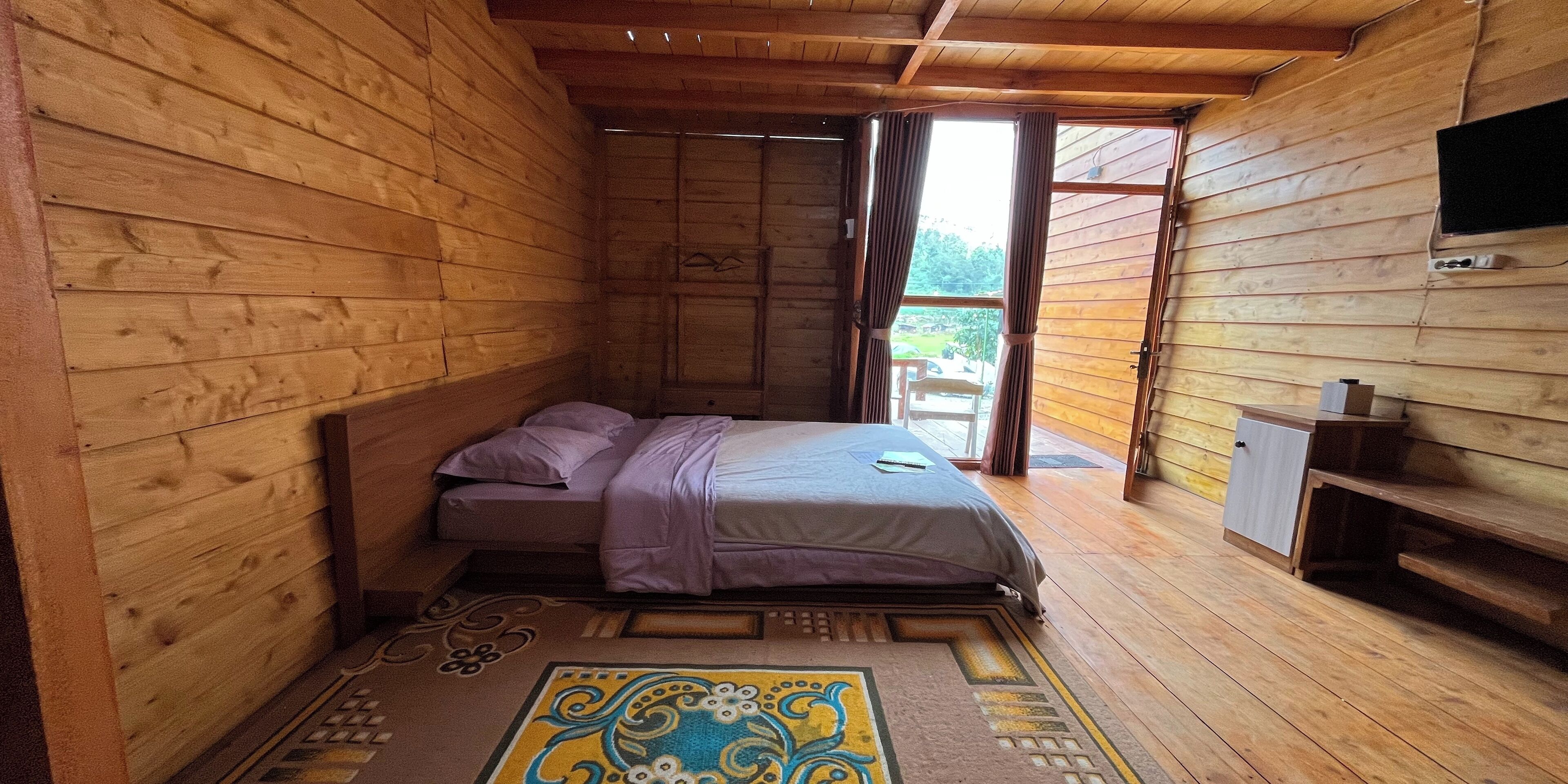 Camera da letto in una baita di legno, con un letto, una piccola credenza e un televisore montato a parete.