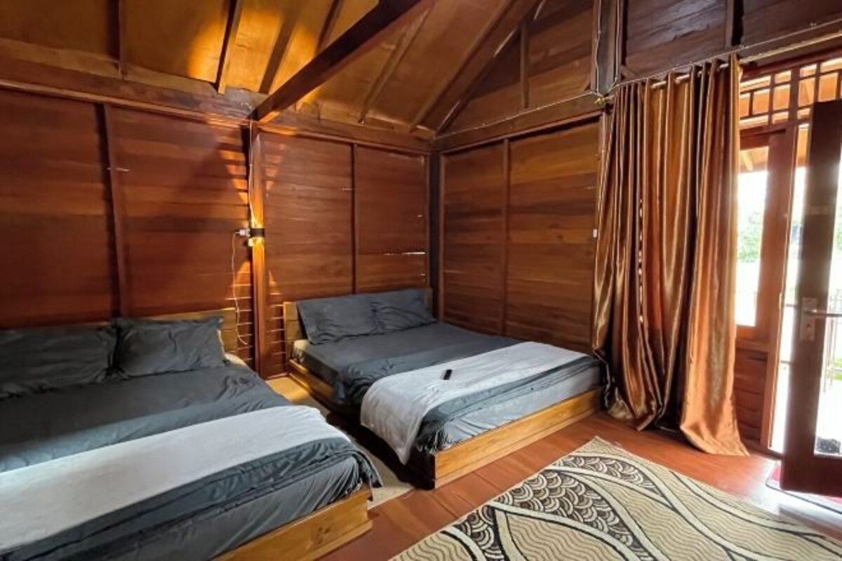 Una habitación de cabaña de madera con dos camas, un tapete estampado y una ventana con cortinas.