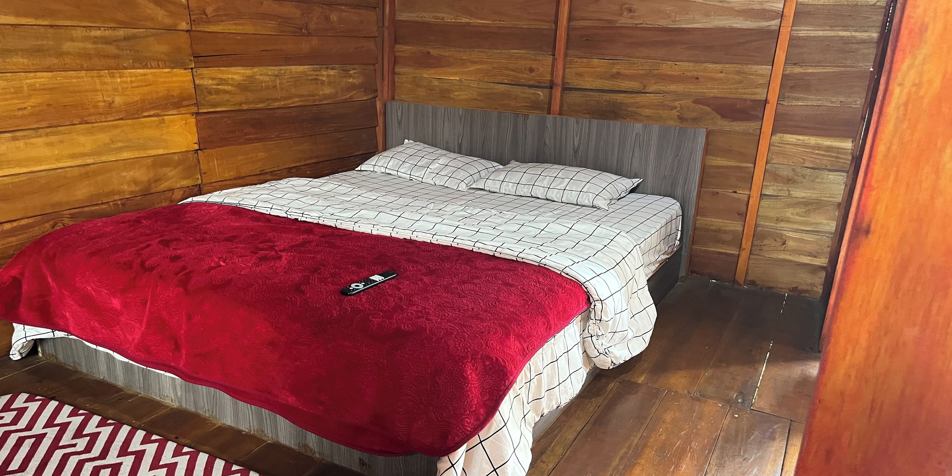A bed with a red blanket, a white and gray checkered bedspread, and a gray headboard.