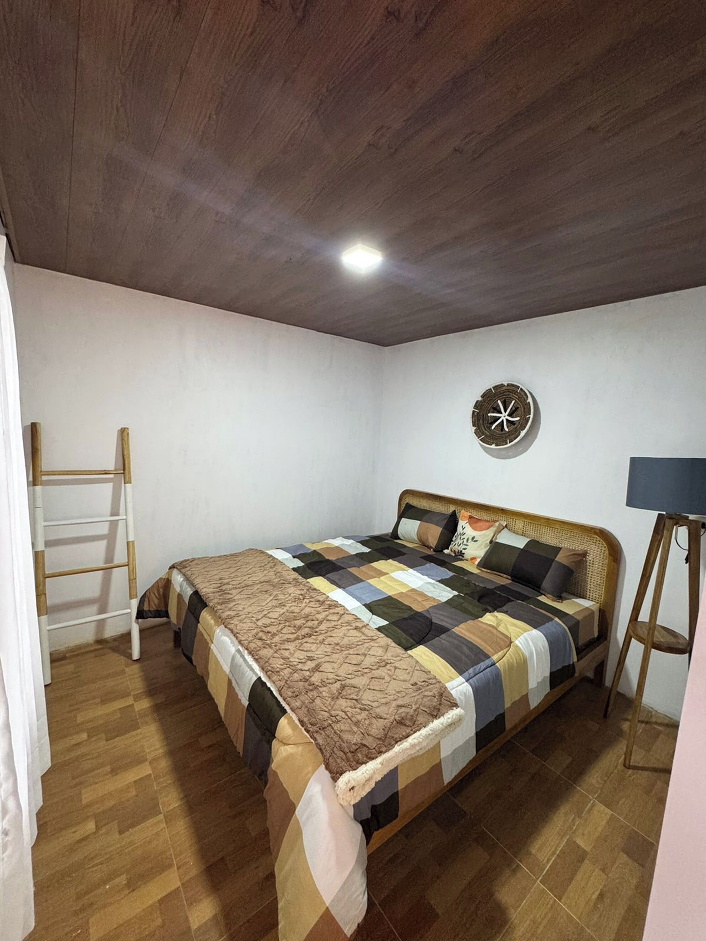 A bedroom with a wooden bed, a ladder, a wall clock, and a standing lamp.