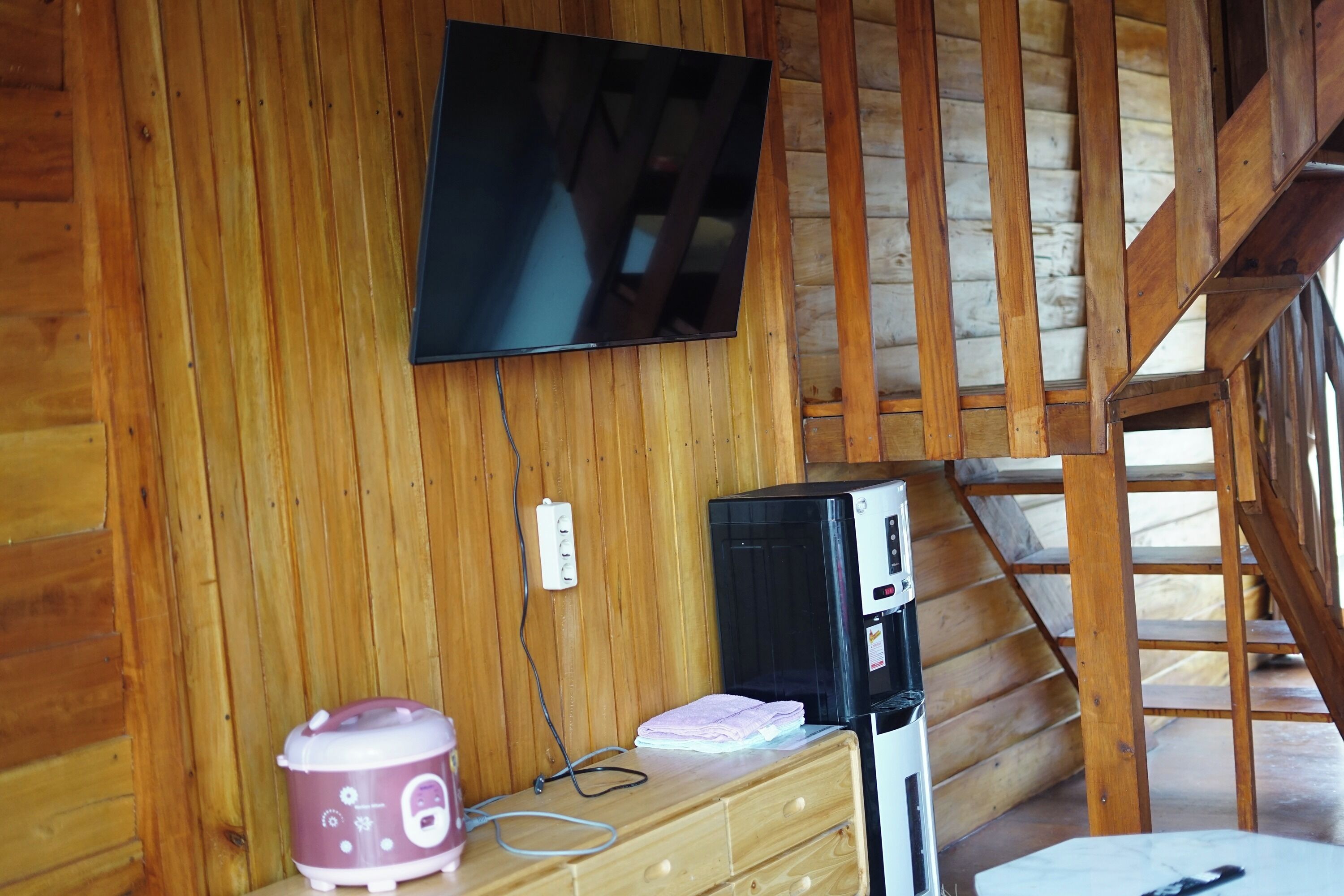 A wooden cabin interior with a television mounted on the wall, a microwave, and a wooden dresser.