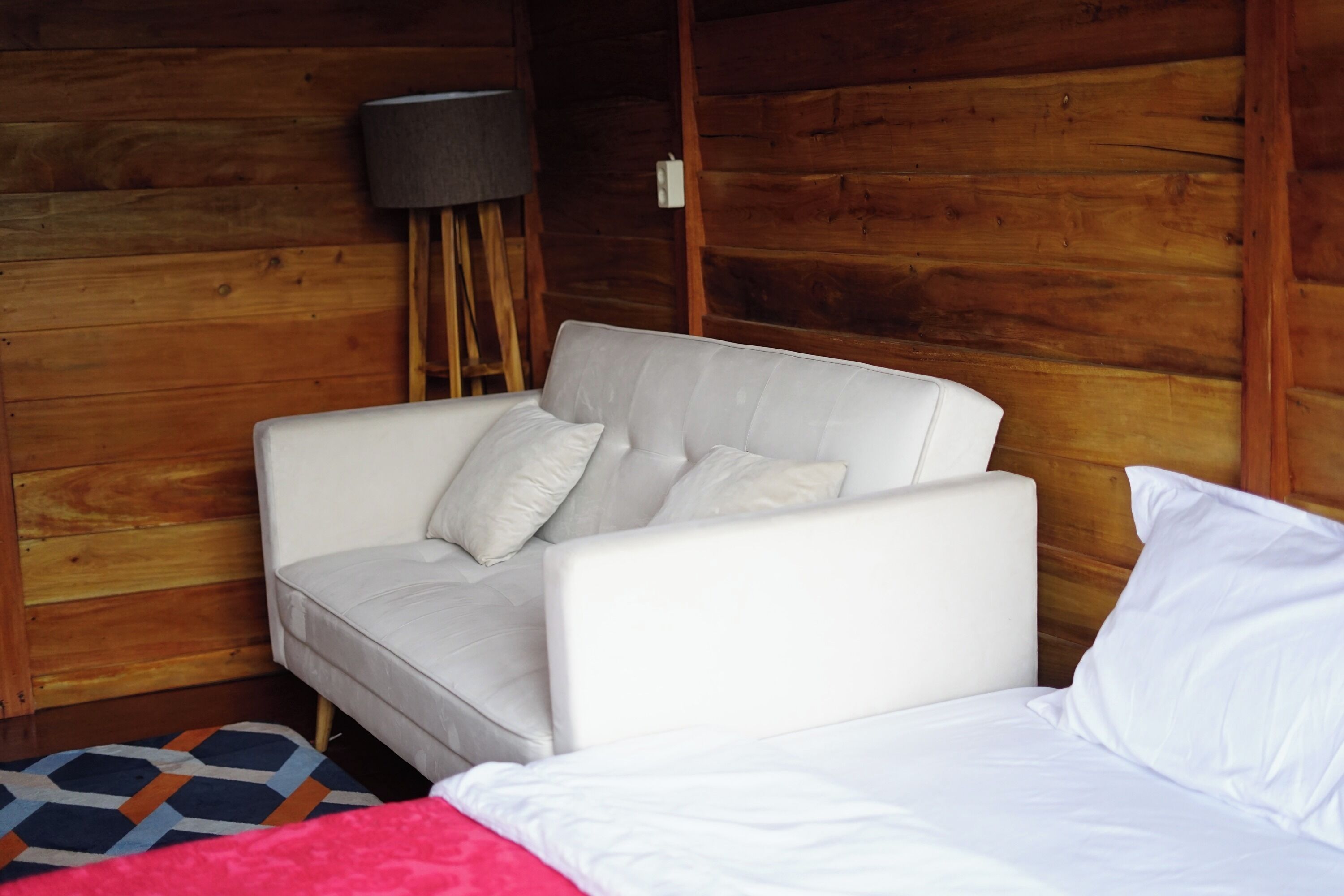 A room with a white sofa, a bed with white bedding, and a patterned rug.