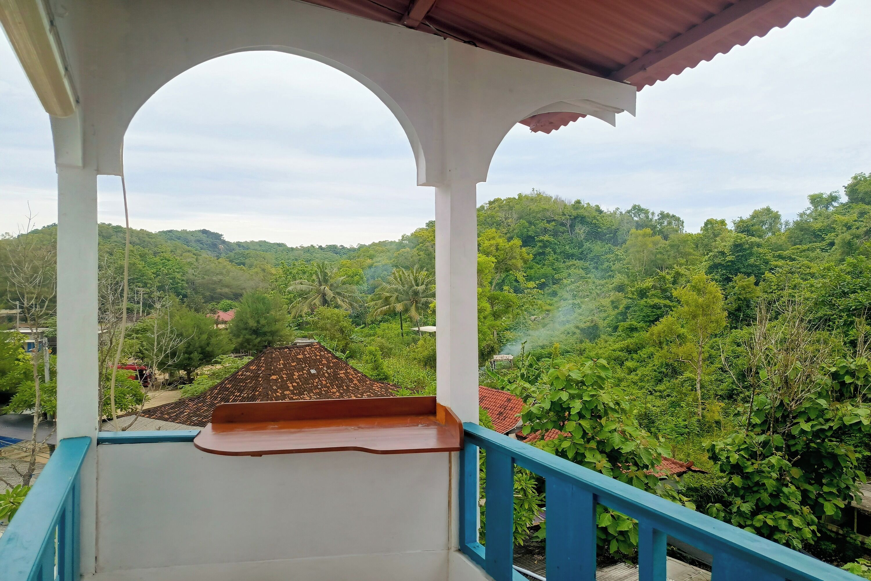 Un balcón con vistas a un paisaje verde exuberante y un edificio distante con techo rojo.