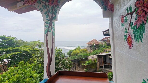 A balcony with a view of the sea, surrounded by lush greenery and a floral archway.