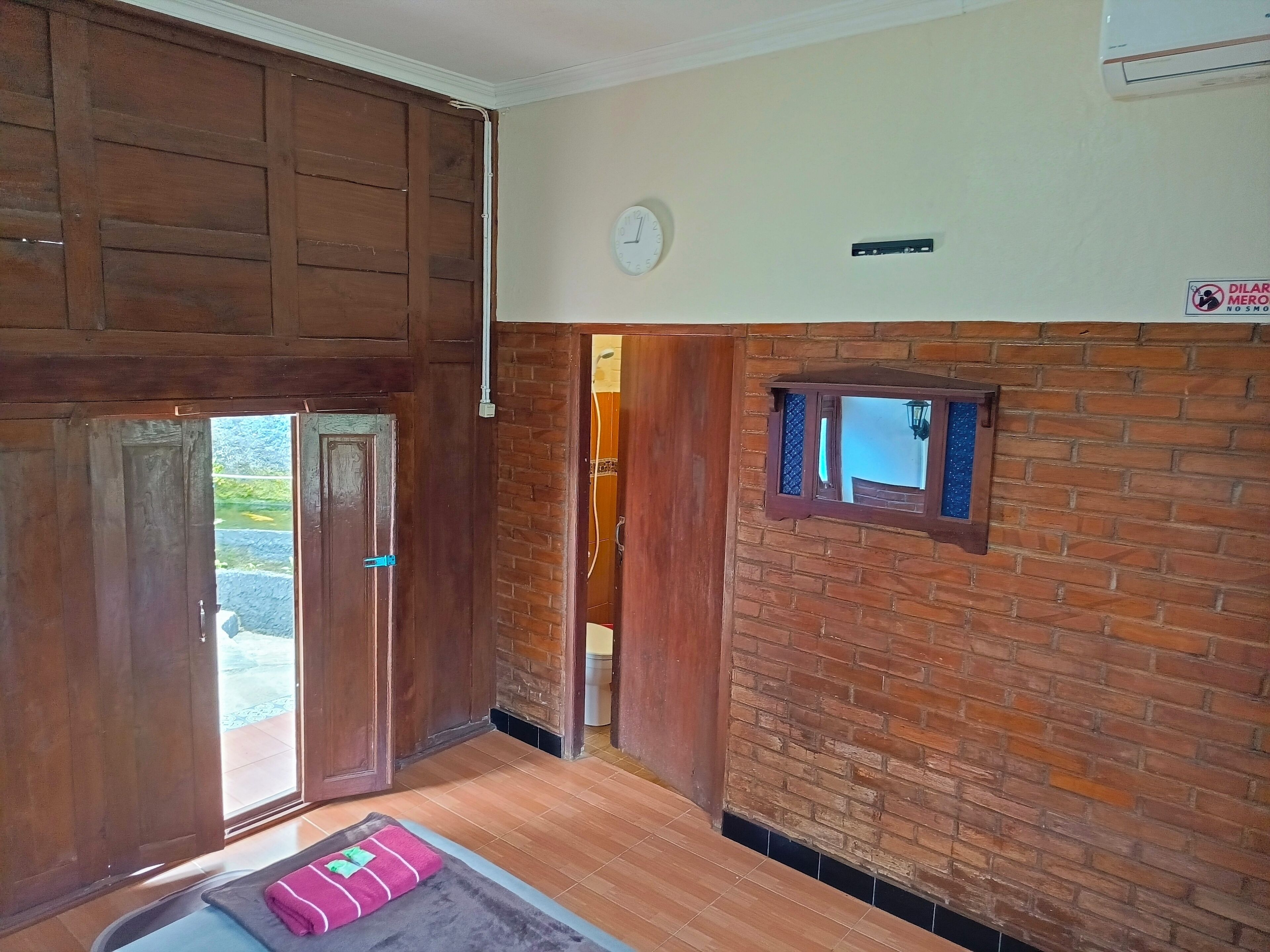 A room with wooden doors, a brick wall, a small window, and a clock on the wall.