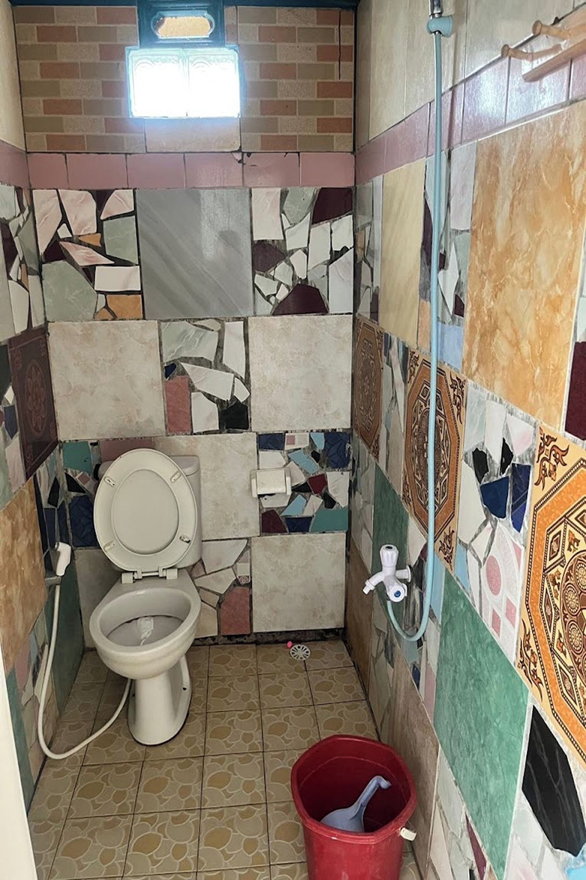 A small bathroom with a toilet, a red bucket, and a shower area.