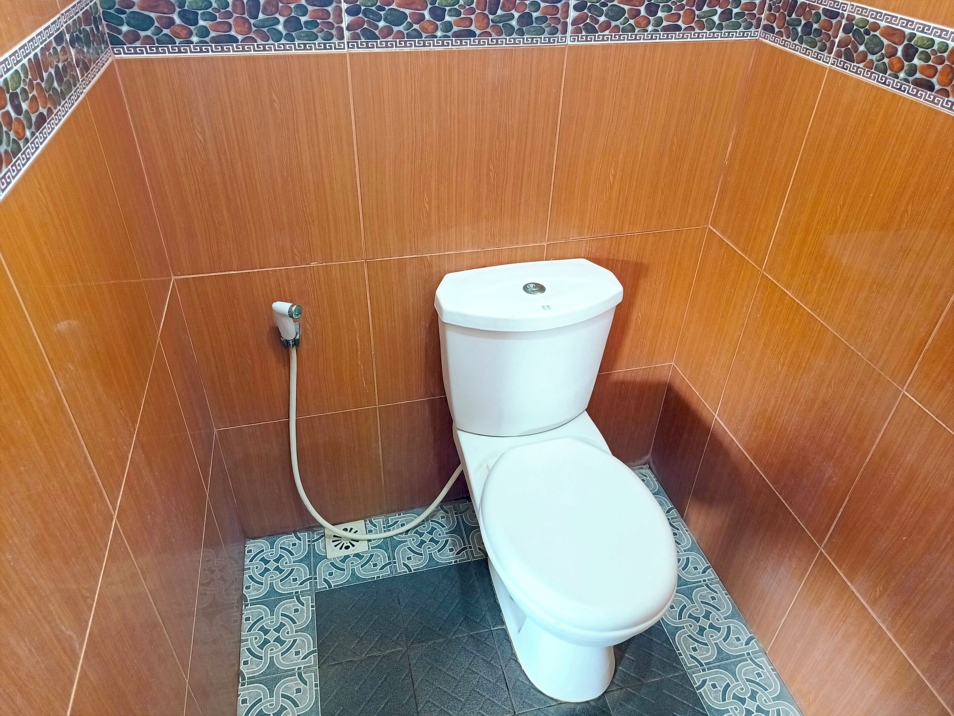 Une petite salle de bain carrelée, avec des toilettes blanches, un flexible de douche et un carrelage au motif.