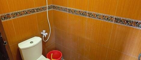 A bathroom with a toilet, a shower hose, and a red bucket.