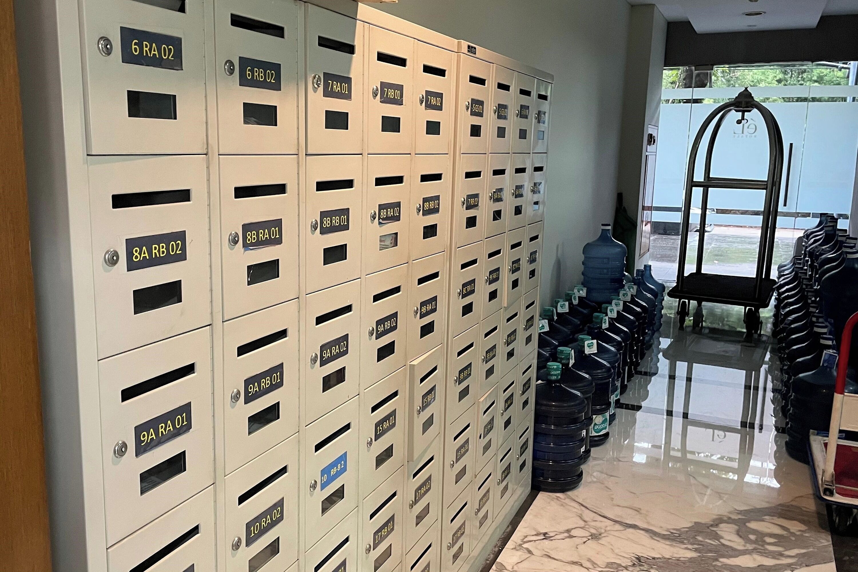 A row of beige storage lockers with labels, a water dispenser, and a cart with bottled water.