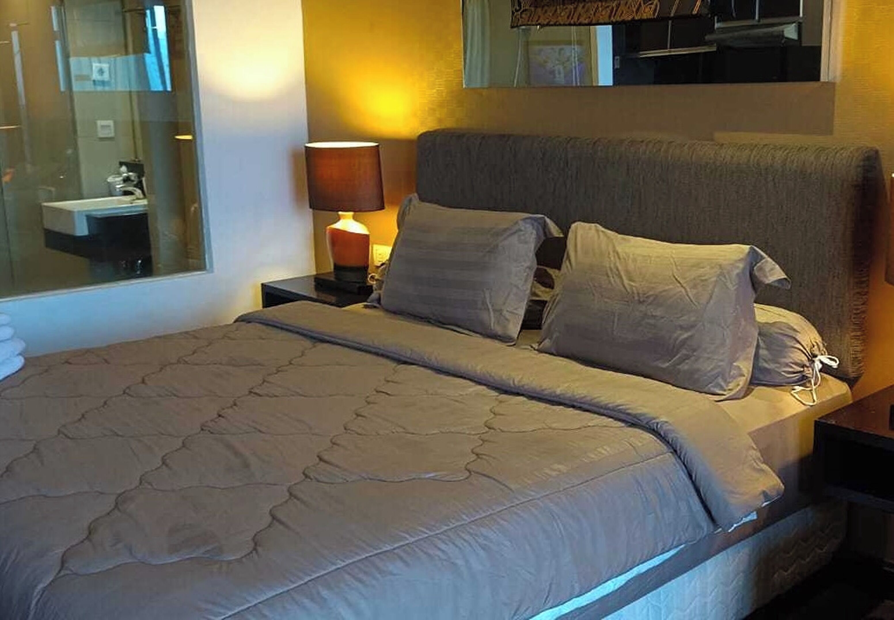 Een bed met een gewatteerde spreideken, twee kussens, een bedlampje en een nachtkastje.