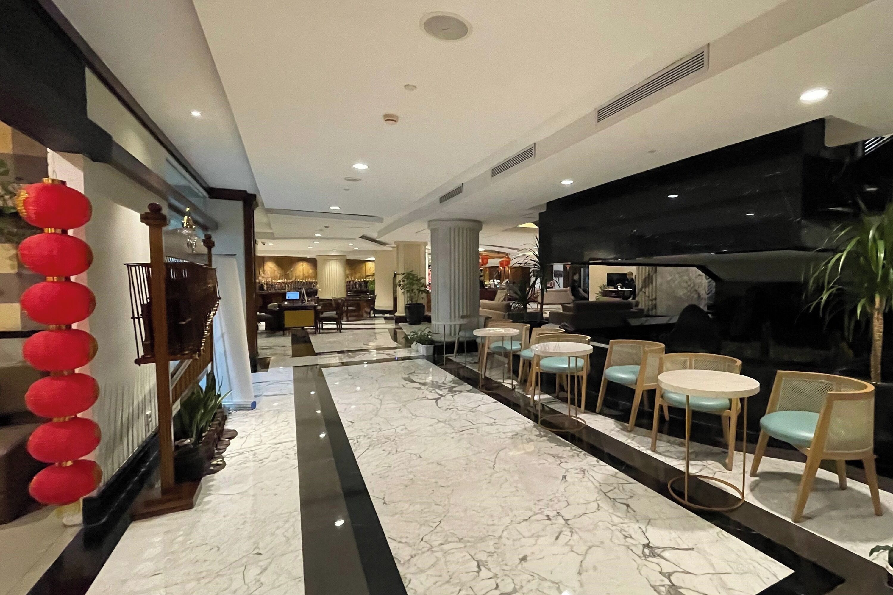 A hotel lobby with a marble floor, seating area with round tables and chairs, a reception desk, and a large black piano.