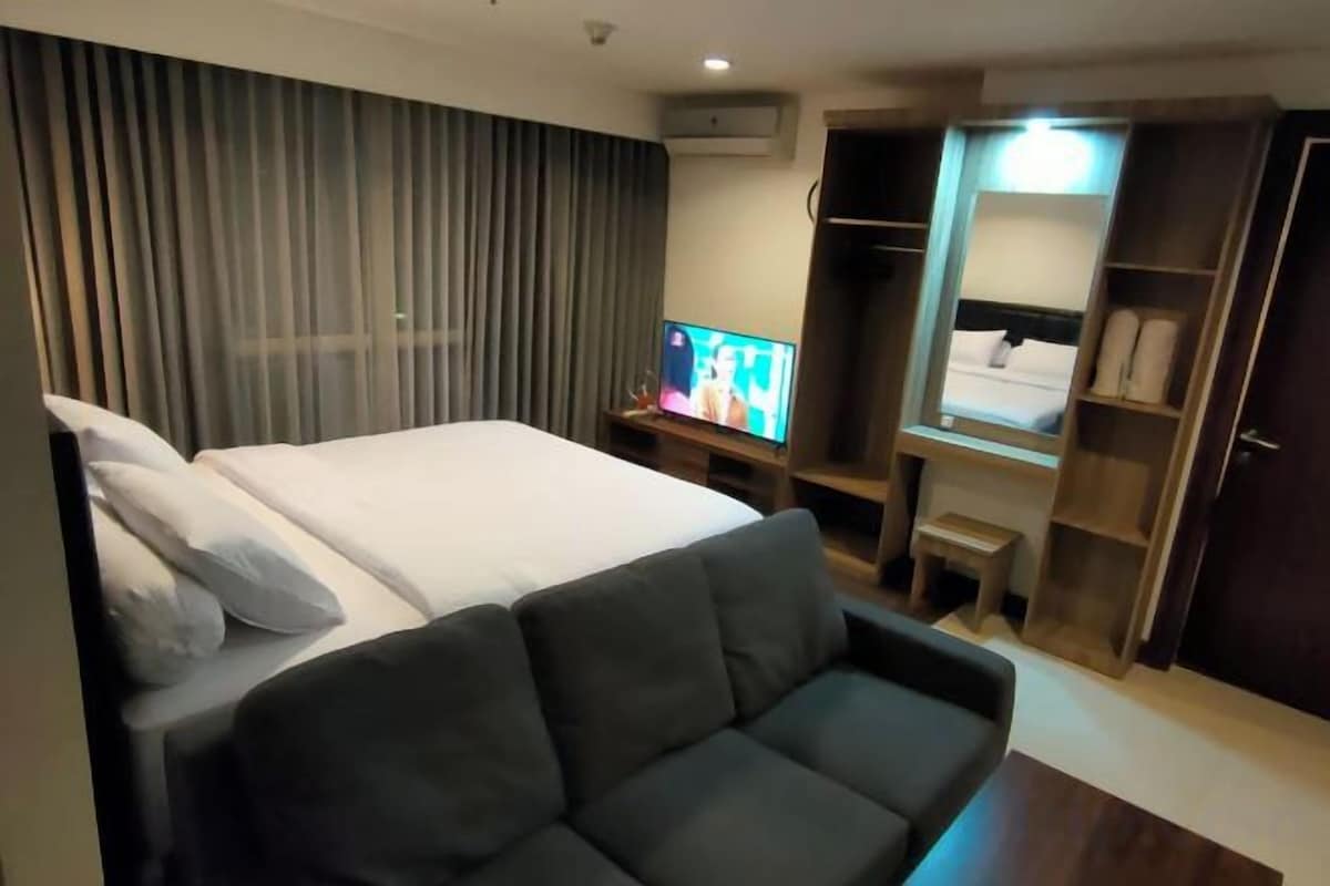 Una habitación de hotel con cama, televisión, sofá y armario.