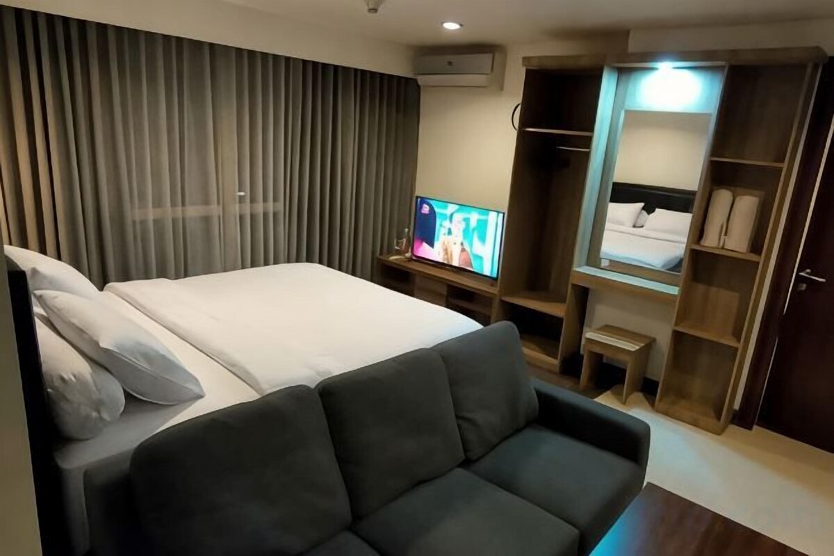 Una habitación de hotel con cama, televisor, sofá, armario y espejo.