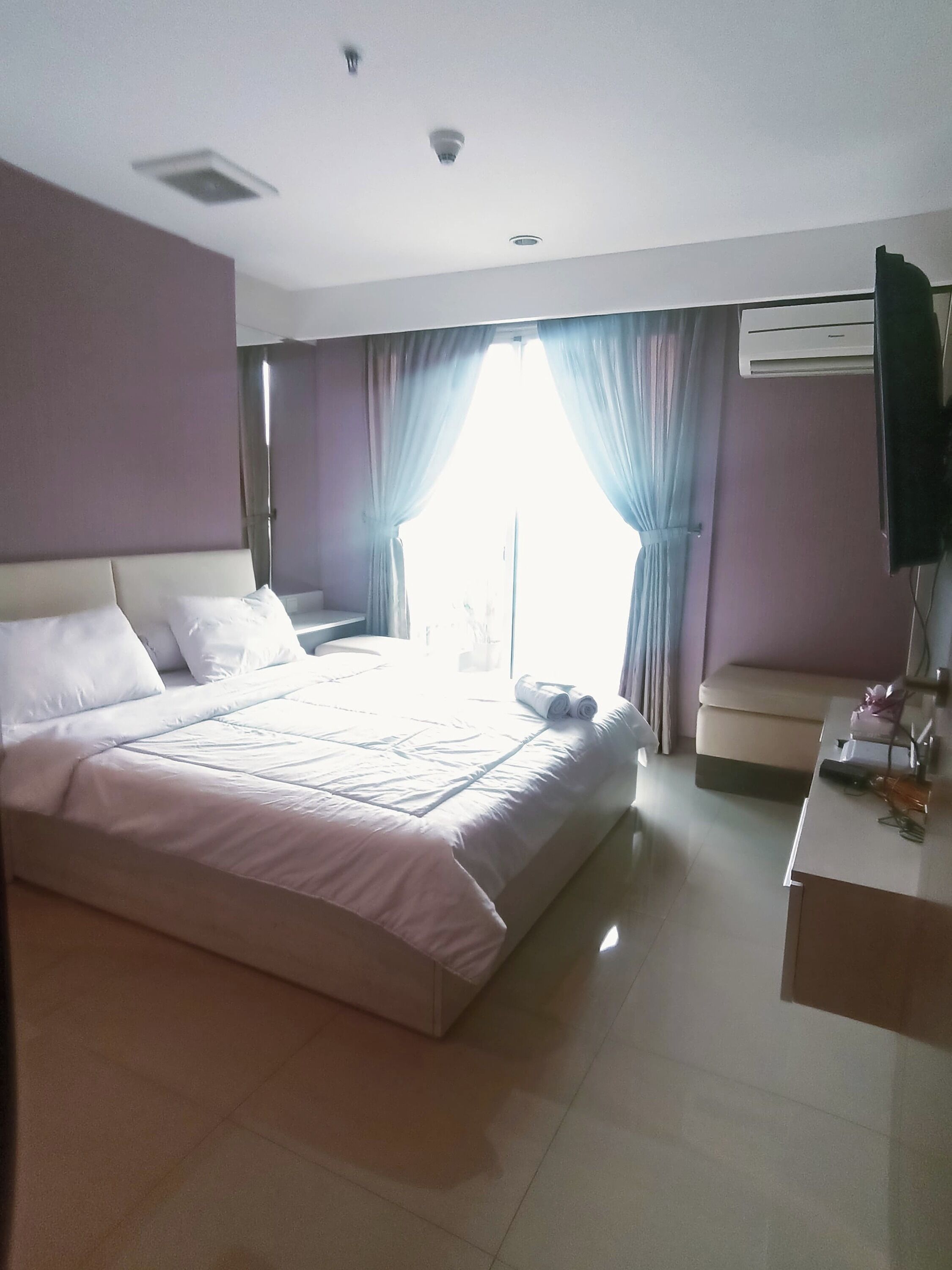 A hotel room with a large bed, a bedside table, a desk, and a window with curtains.