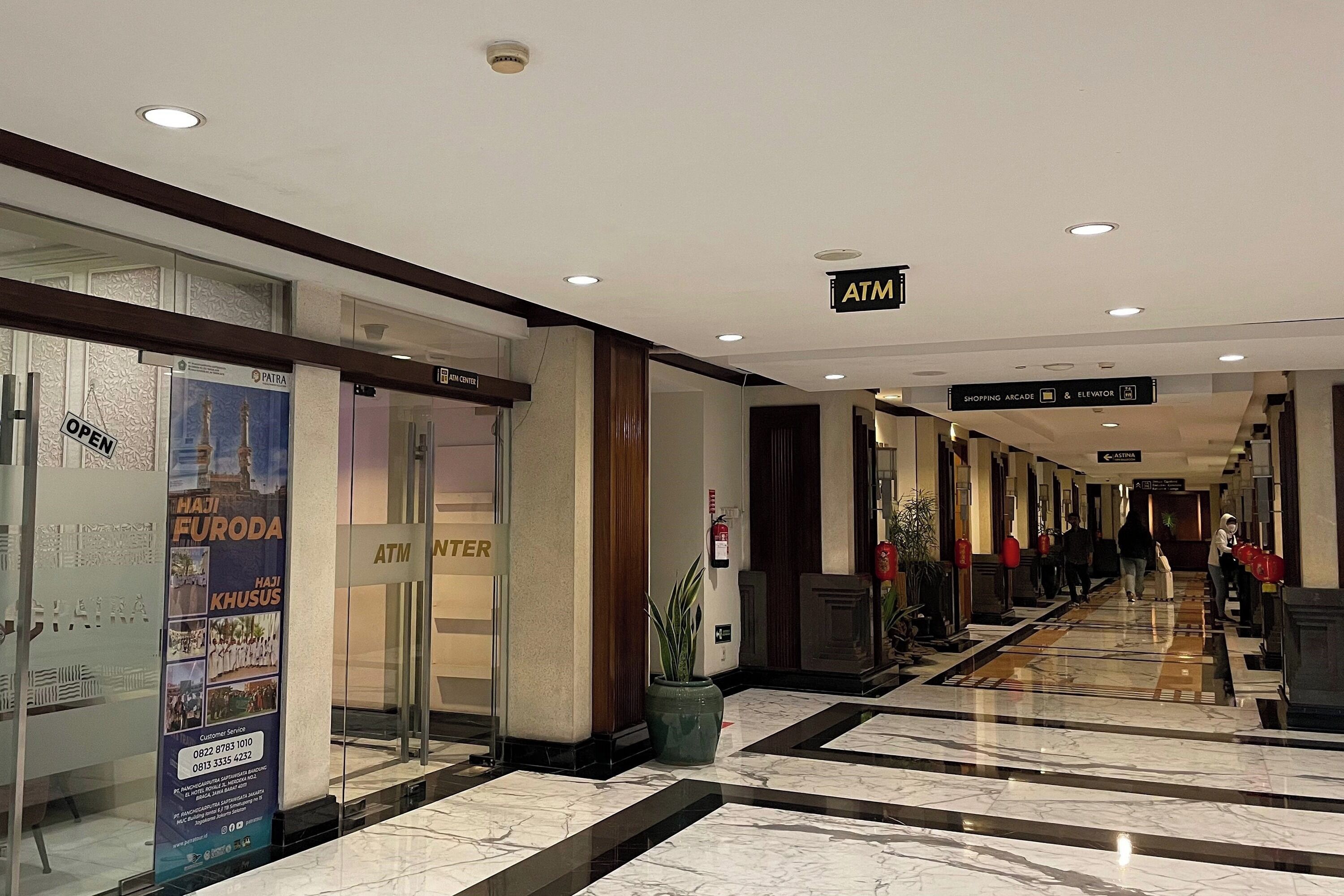 A hotel corridor with an ATM, a shopping arcade, and an elevator sign.