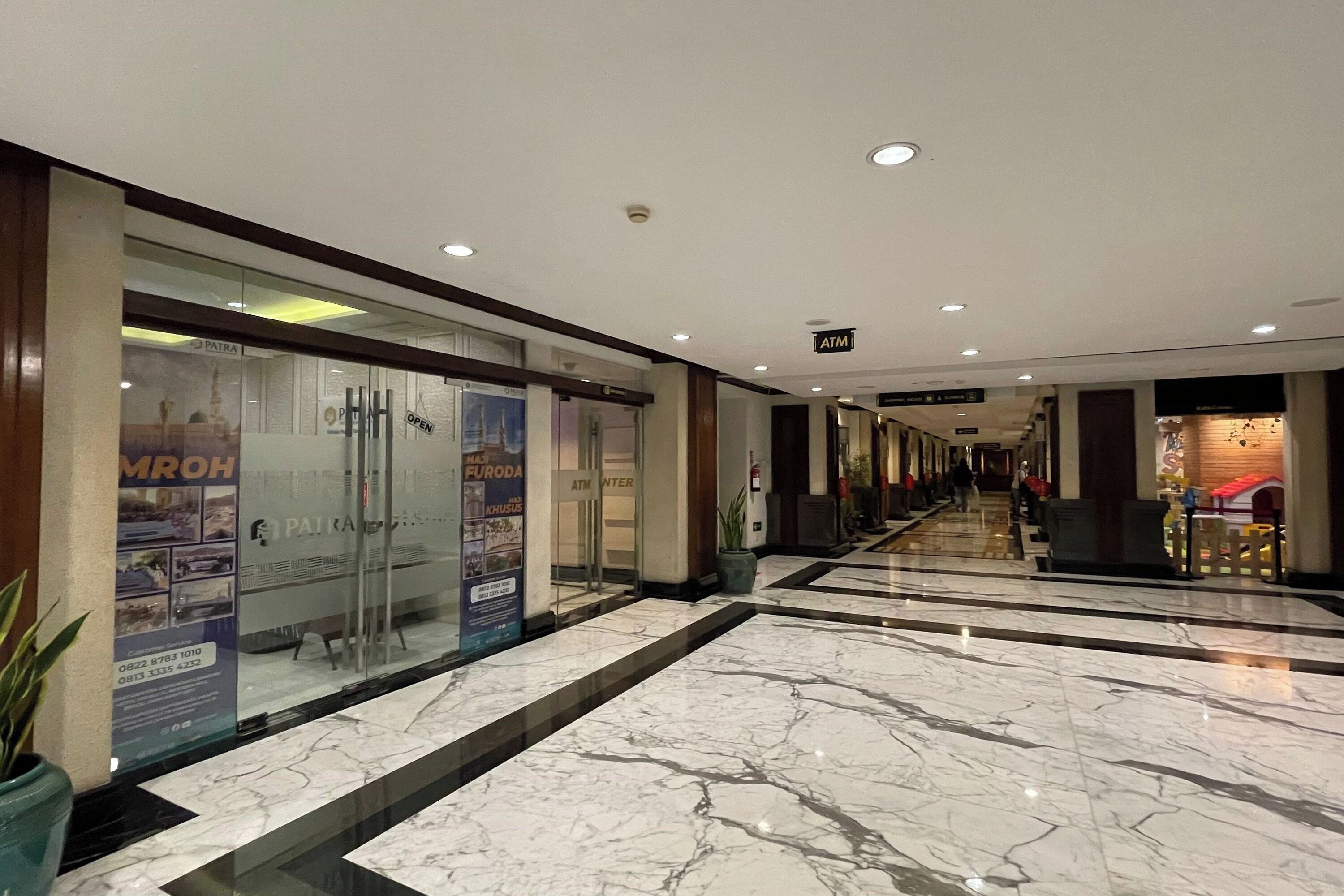 A corridor with marble flooring, glass doors, and signs for an ATM and a restaurant.