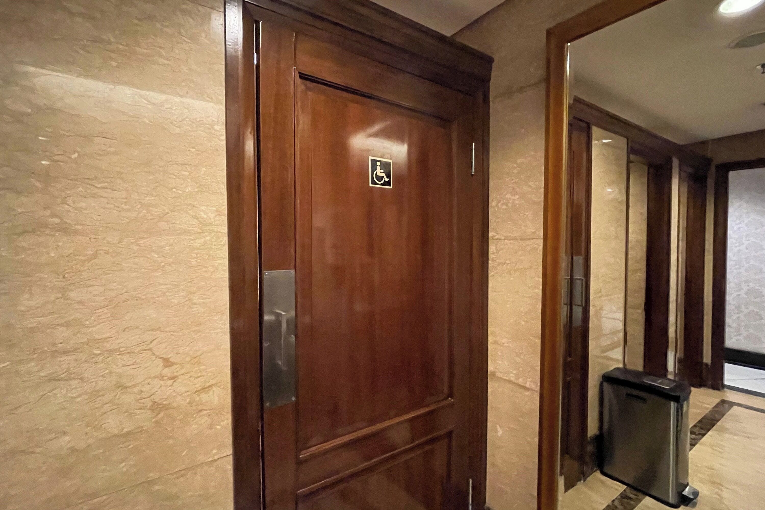 Una puerta de madera con el símbolo de accesibilidad para personas con discapacidad, un bote de basura y una pared de mármol.
