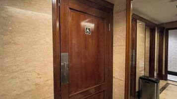Uma porta de madeira com o símbolo de acessibilidade, um contentor de lixo e uma parede de mármore.