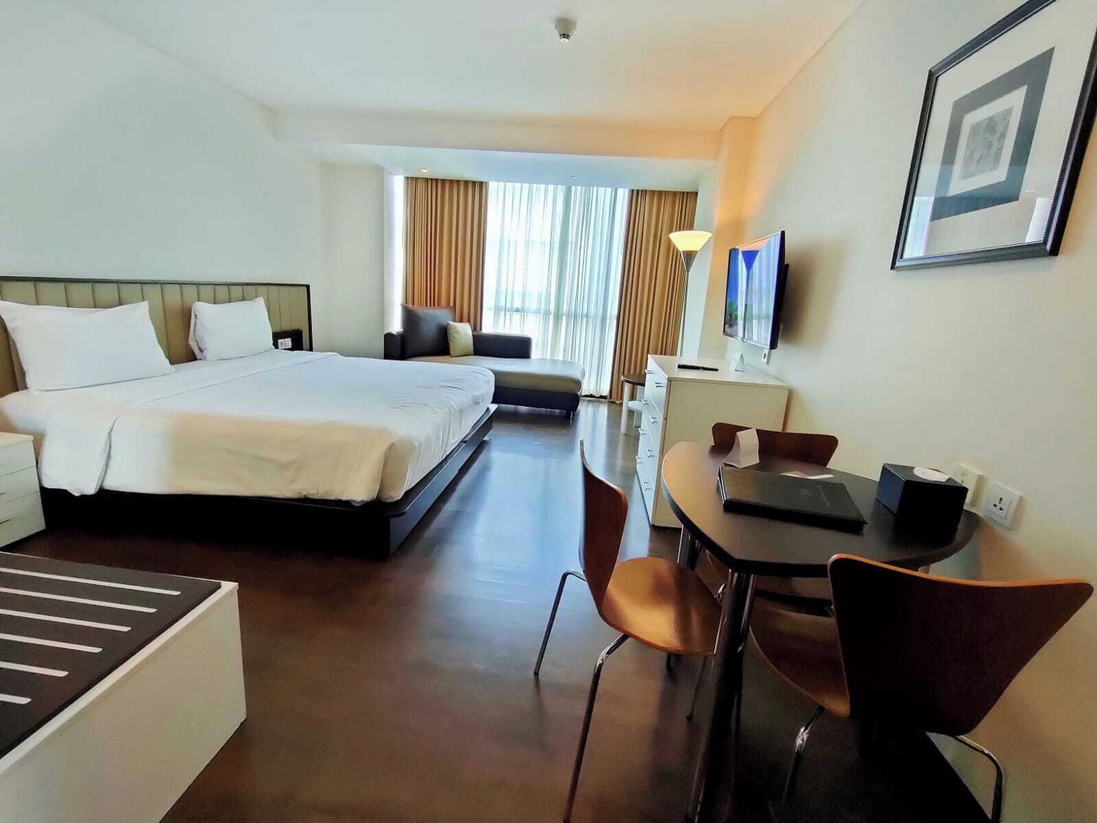 Ein Hotelzimmer mit Bett, Schreibtisch mit Stuhl, Fernseher und einem gerahmten Bild an der Wand.