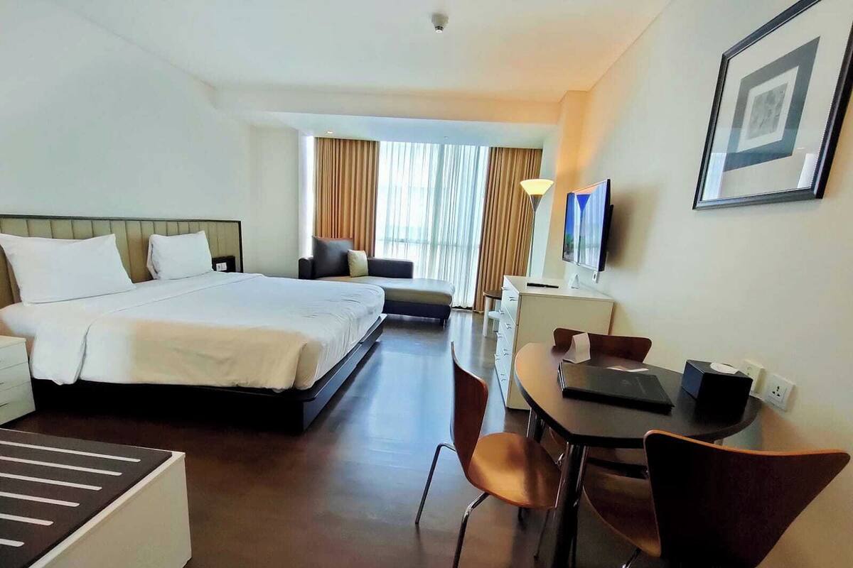 Une chambre d’hôtel avec un lit, un bureau et une chaise, une télévision et un tableau encadré au mur.