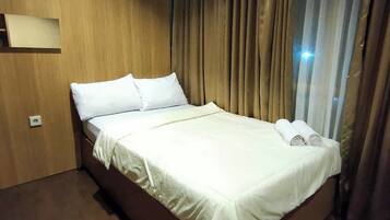 A neatly made bed with white linens and pillows, a wooden headboard, and a large window with curtains.