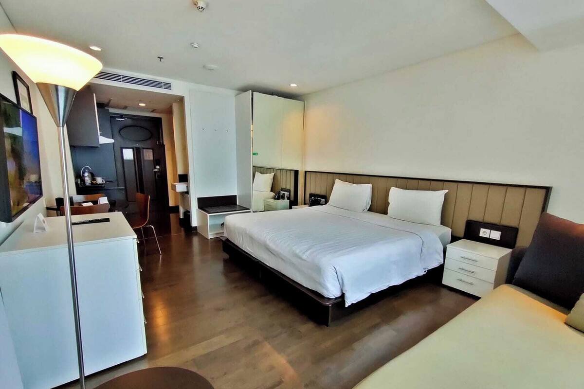 A hotel room with a bed, bedside tables, a desk, a chair, and a small refrigerator.