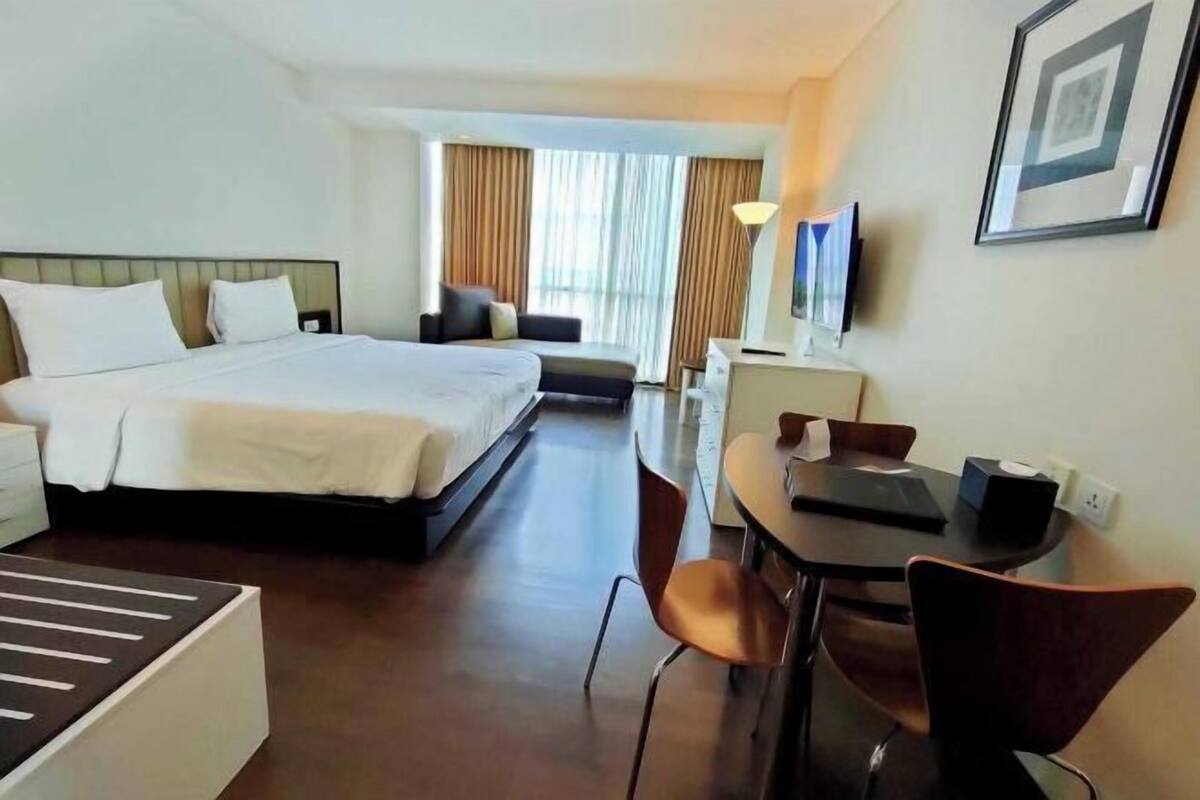 A hotel room with a bed, a desk, a chair, a sofa, and a TV.