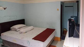 A bedroom with a bed, pillows, and a blanket. There is a water cooler and a small table with a chair.