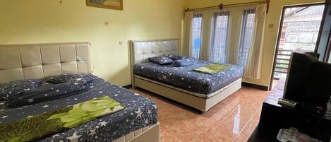 A hotel room with two beds, a small desk, and a window with curtains.