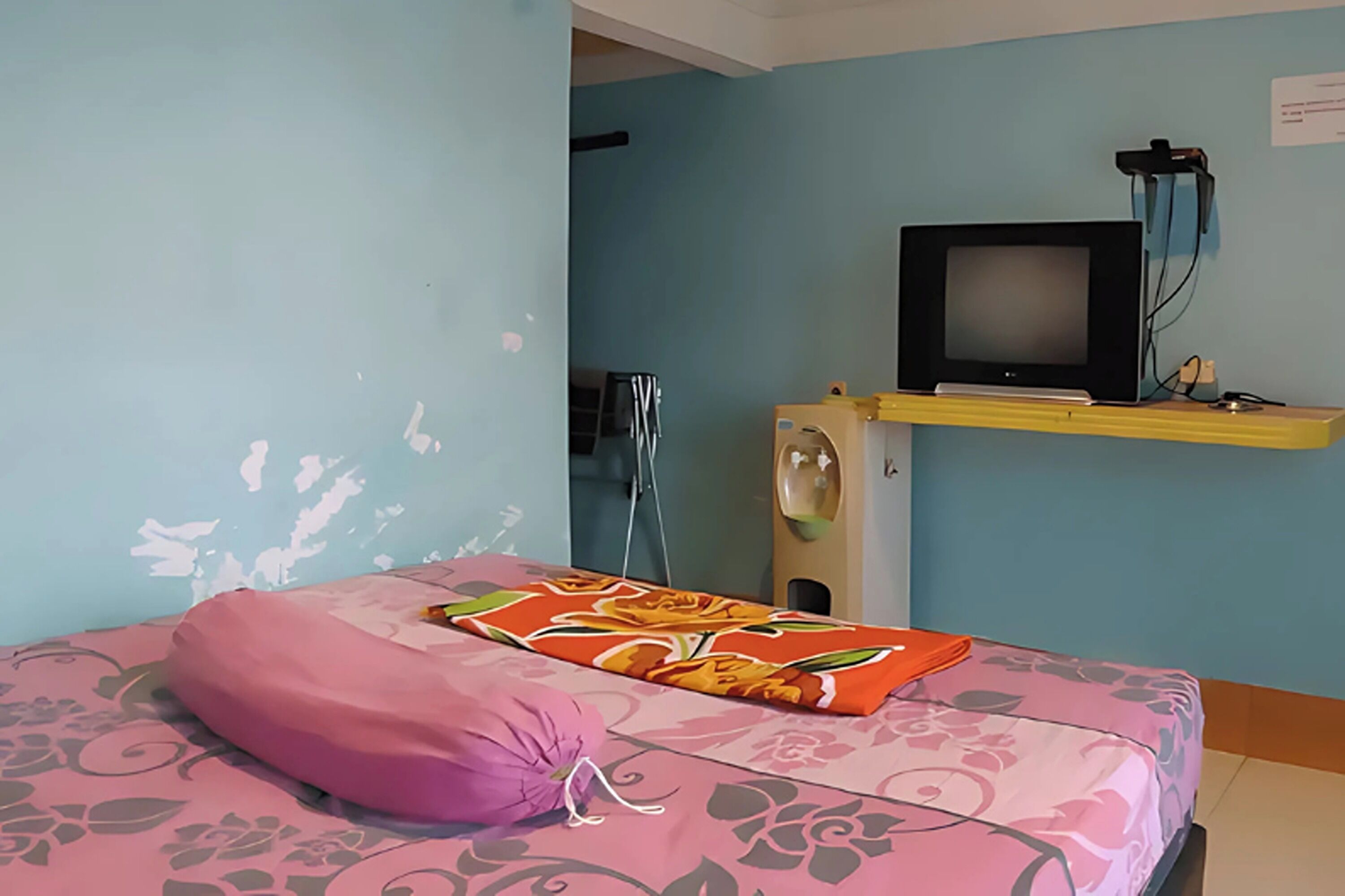 A room with a bed, a television on a stand, and a wall-mounted sink.