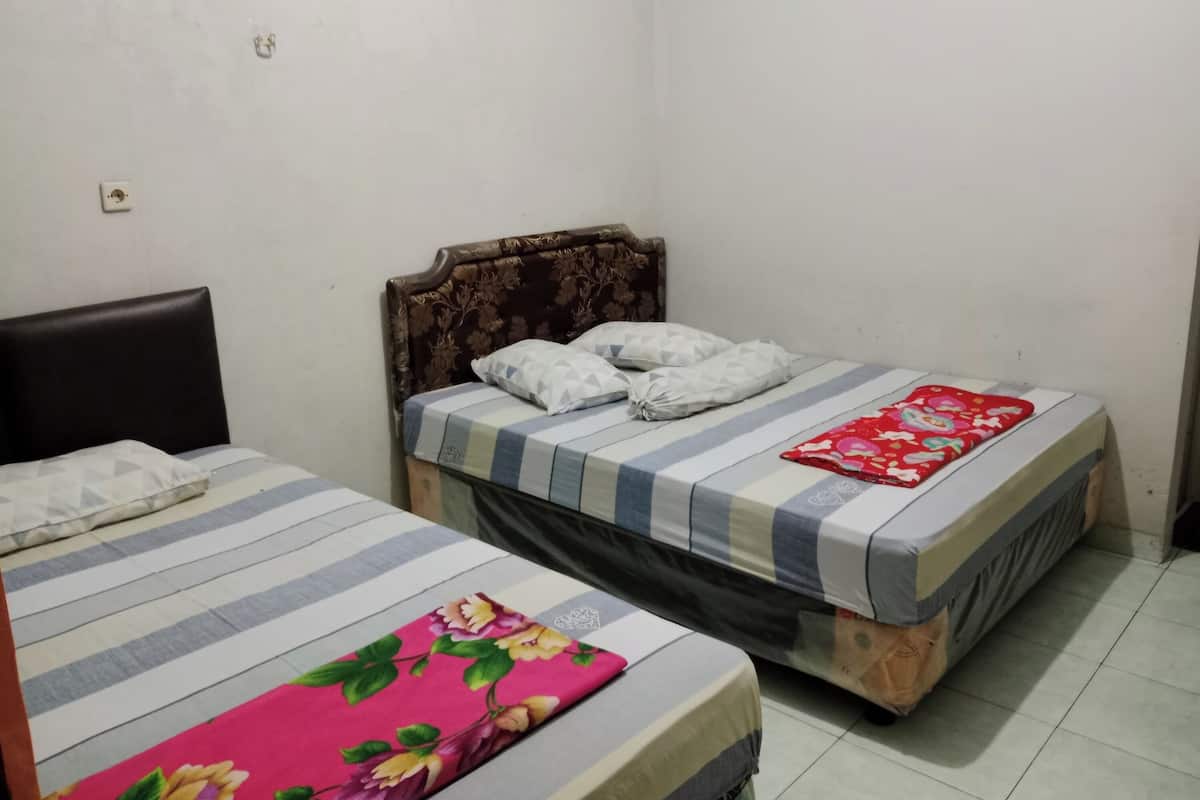 Een kamer met twee bedden, waarvan één een bloemenprint sprei heeft en de ander een gestreepte sprei.