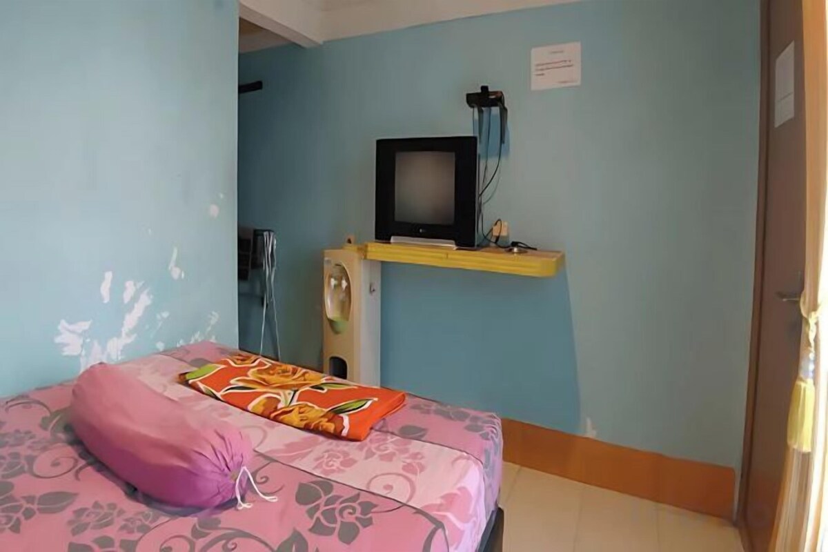 Ein Zimmer mit einem Bett, einem Fernseher auf einem Regal und einer Tür.