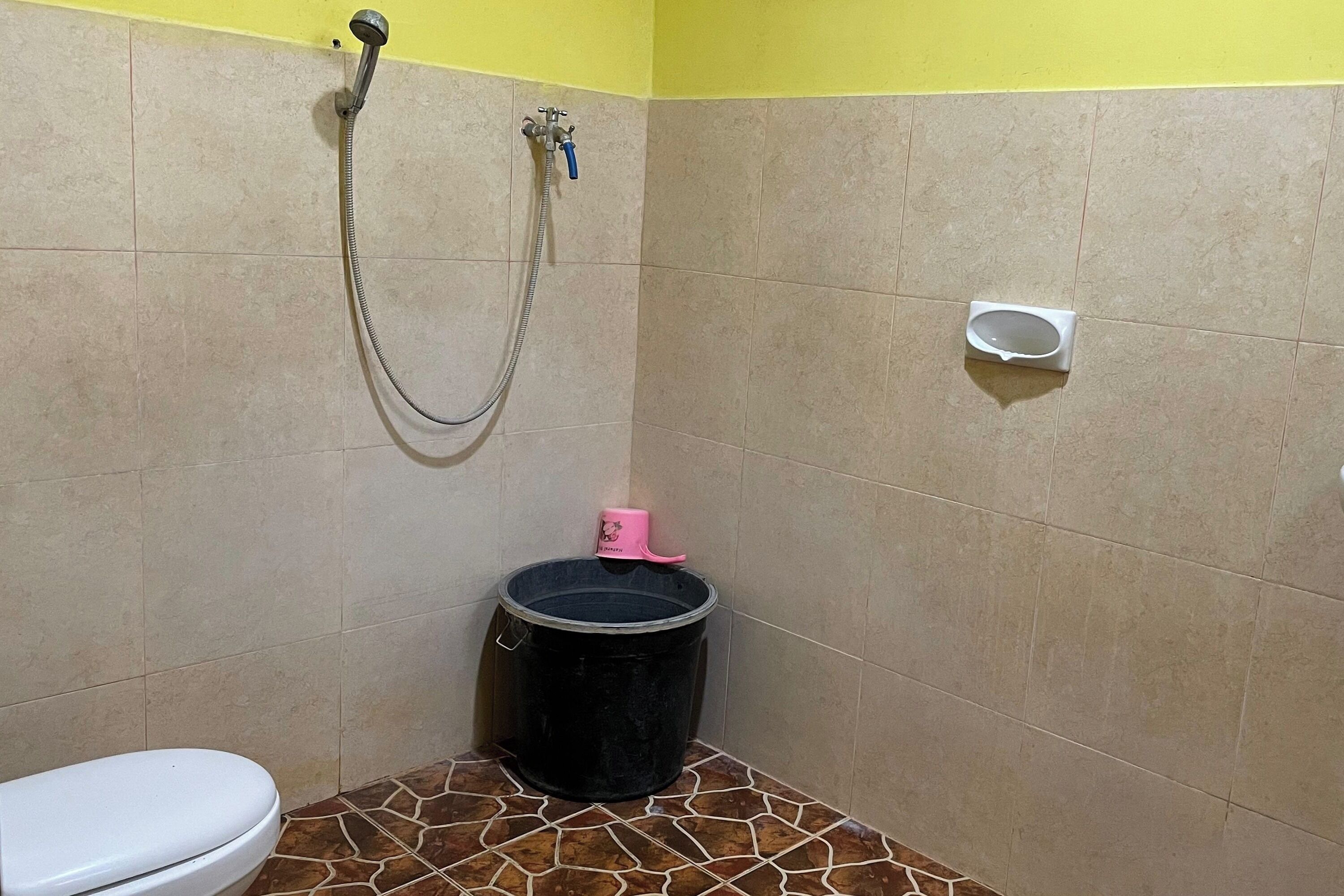 A small bathroom with a toilet, a shower, and a black bucket.