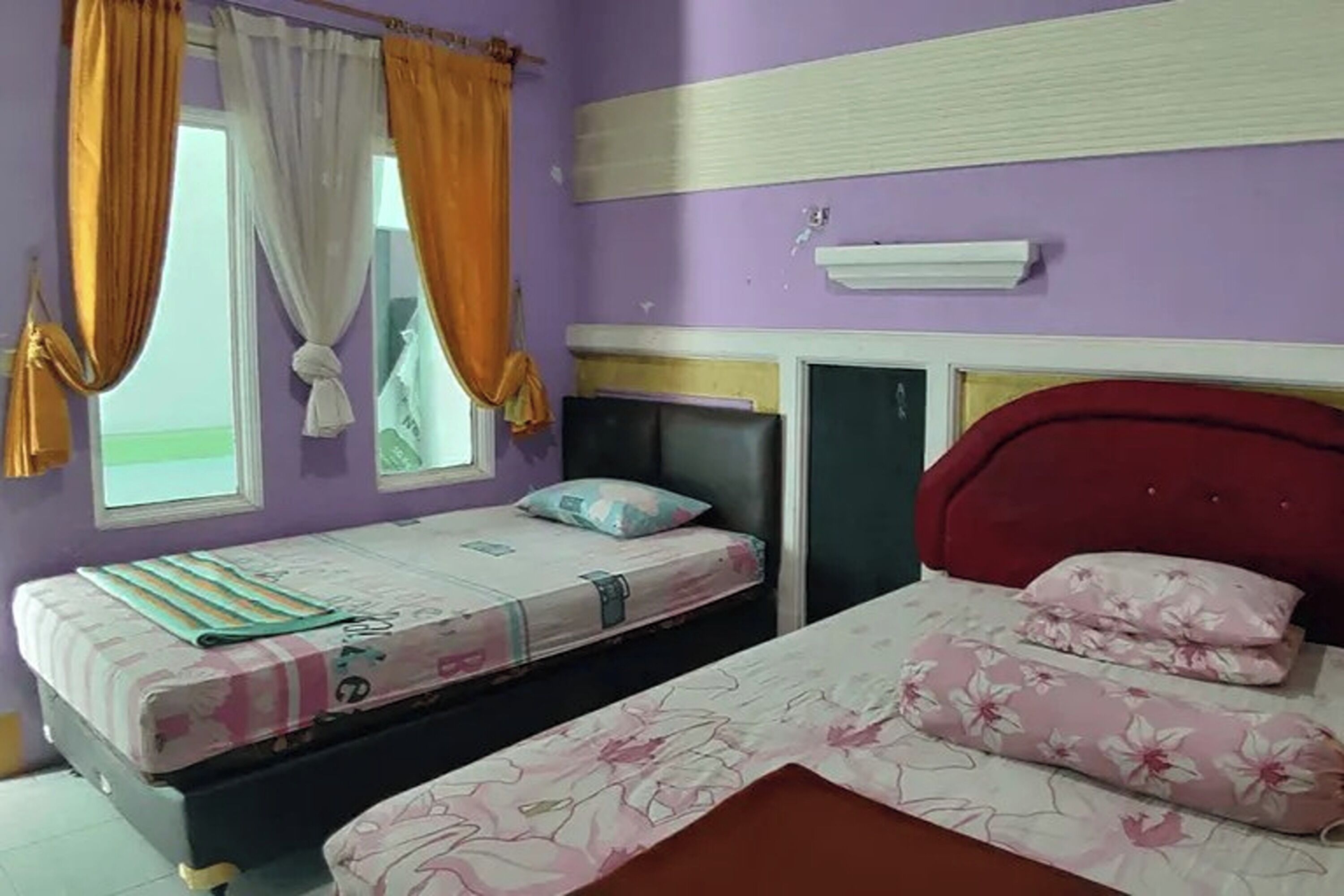 A bedroom with two beds, purple walls, and a window with curtains.