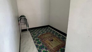 Een kleine, smalle kamer met een metalen ladder tegen de muur, een kamerbreed tapijt met een patroon op de vloer en een effen witte muur.