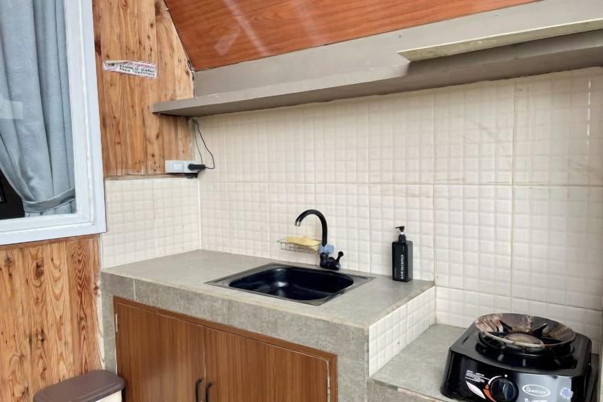A compact kitchen with a sink, countertop, and a portable stove.