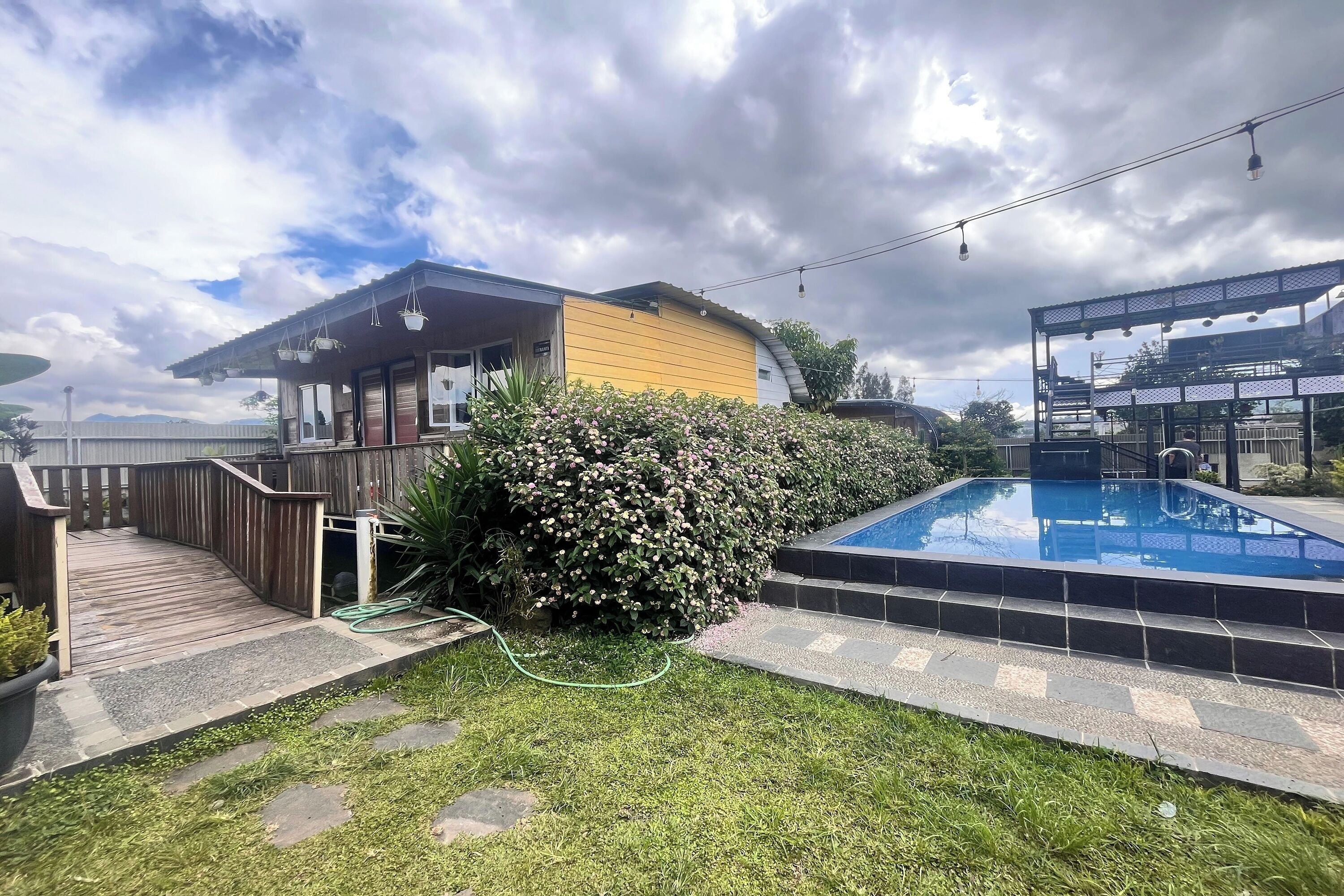 Un jardin avec une terrasse en bois, une piscine et une maison à l’extérieur jaune.