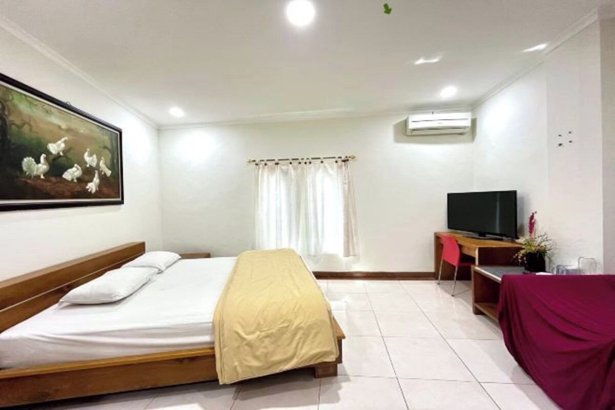 Habitación de hotel con cama, televisión, escritorio y ventana con cortinas.